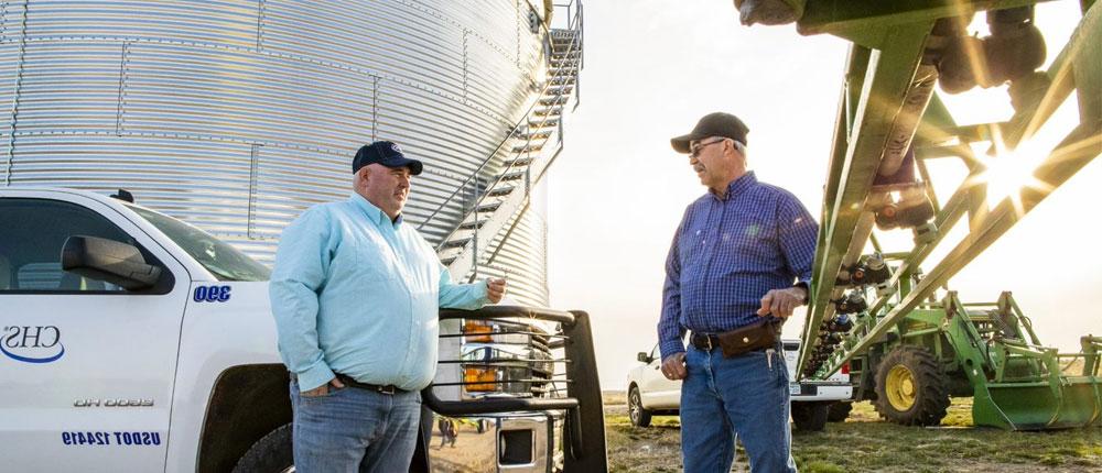 农民和澳门皇冠赌场平台家在农用设备和粮仓旁交谈 